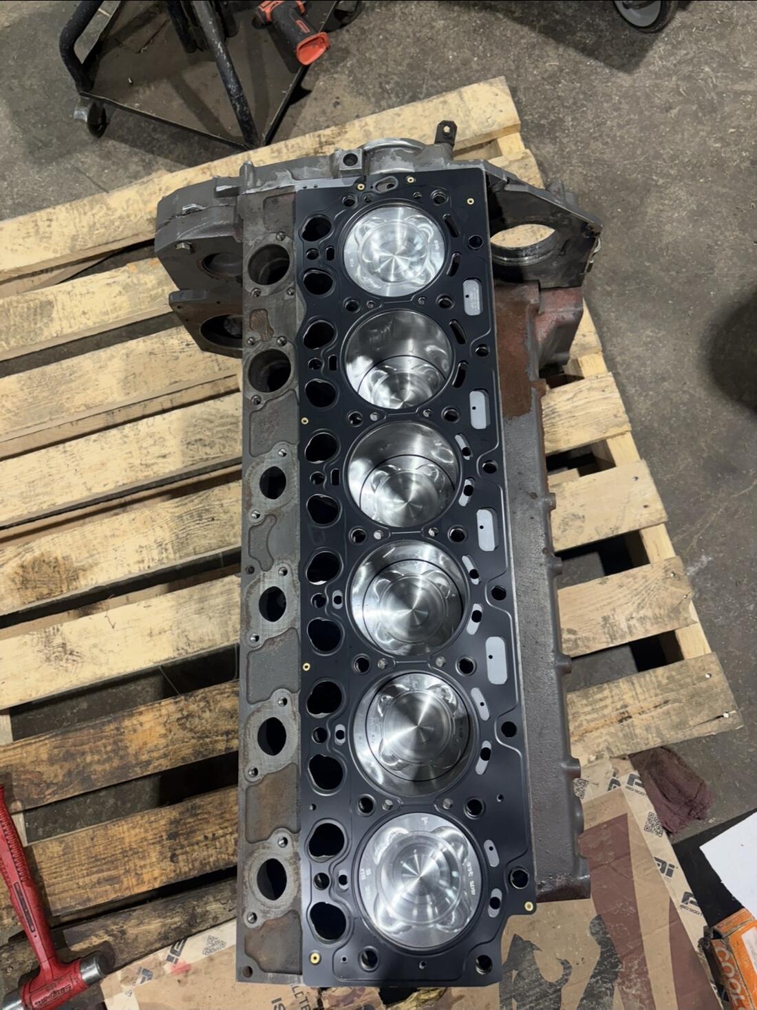 Six-cylinder engine block with new pistons, sitting on a pallet